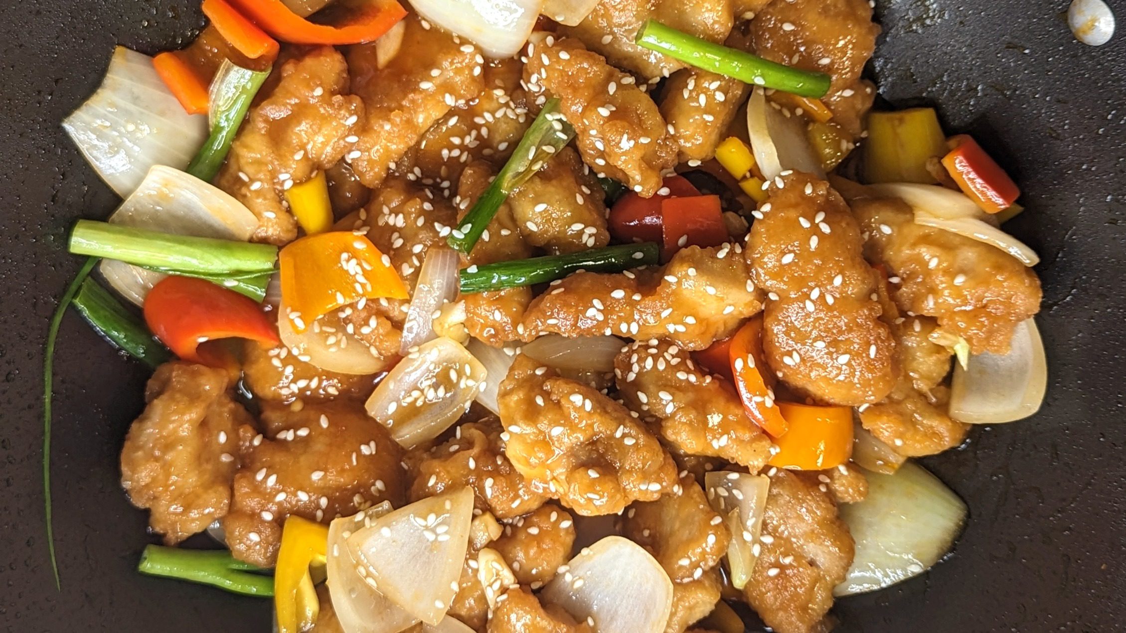 Crispy sweet and sour chicken in a wok with bell peppers and sesame seeds