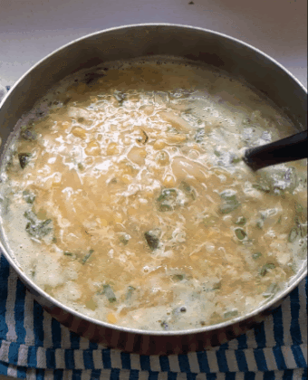 Chinese chicken corn soup bubbling in a pot while cooking with egg ribbons forming