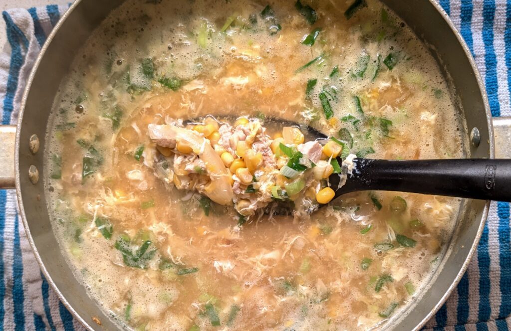 Chinese chicken corn soup in a pot with a ladle showing chicken, corn and green onions