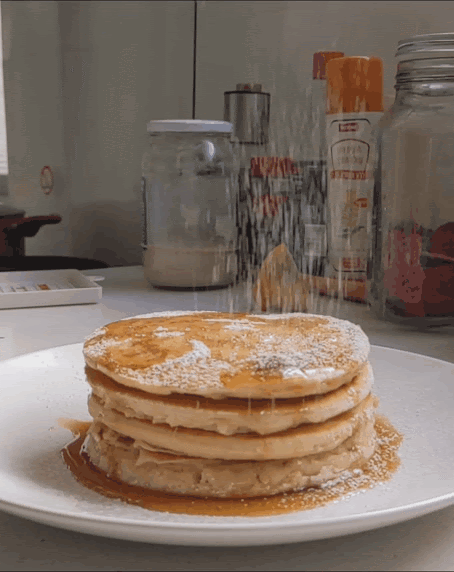 Stack of classic pancakes with powdered sugar falling and maple syrup dripping