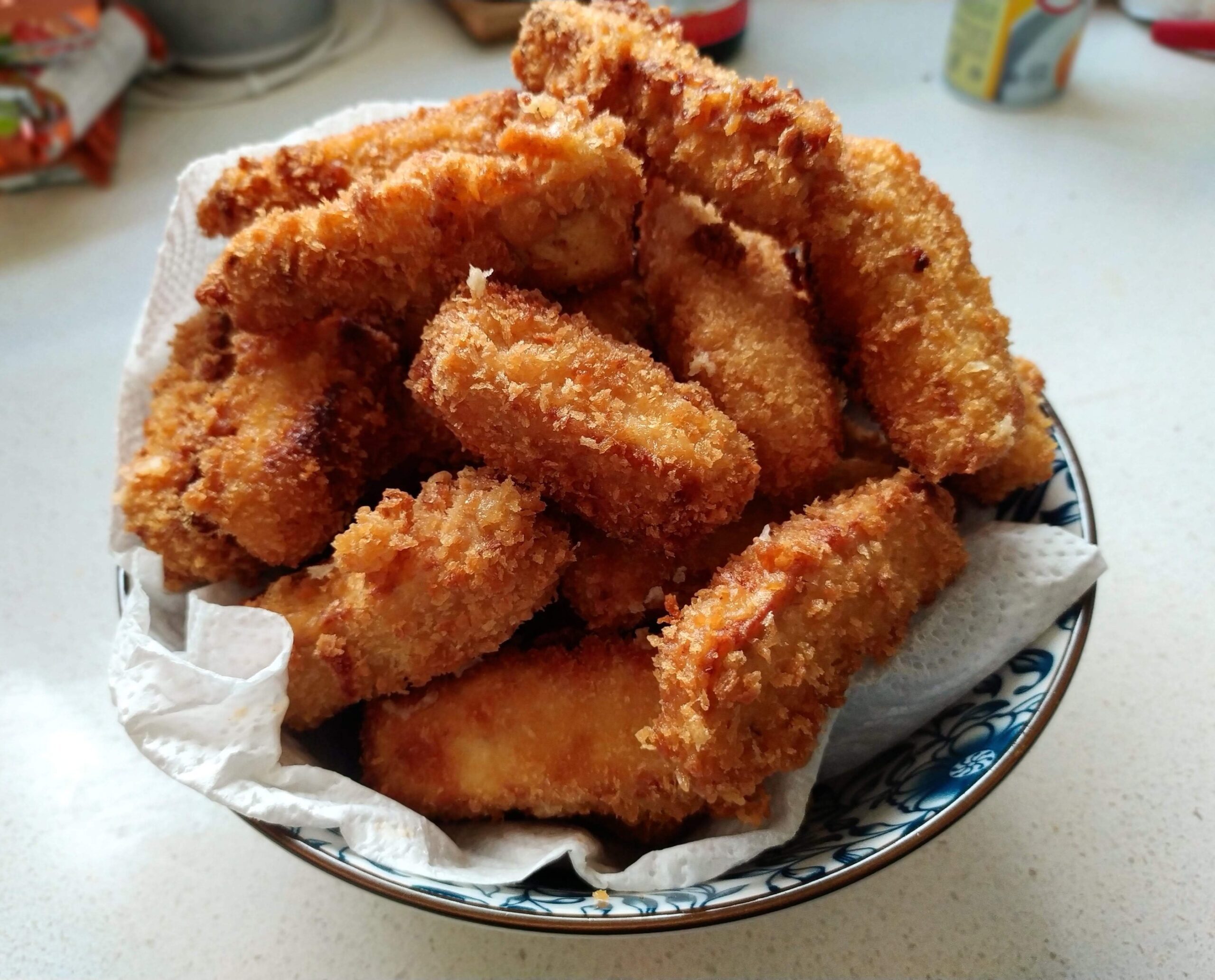 Crispy fried tofu fingers piled in a bowl lined with paper towel