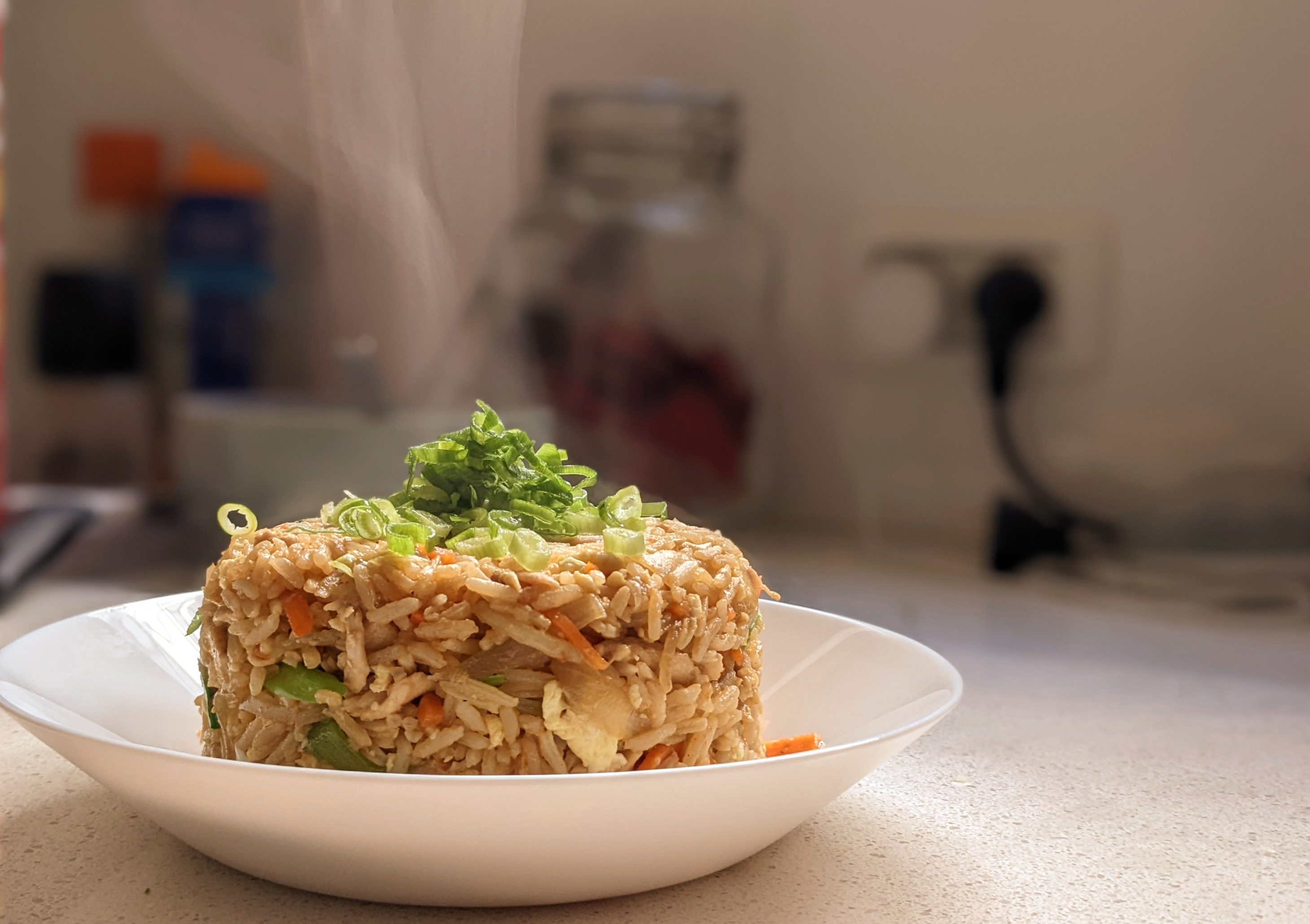 Chicken fried rice served in a white bowl with steam rising and green onions on top