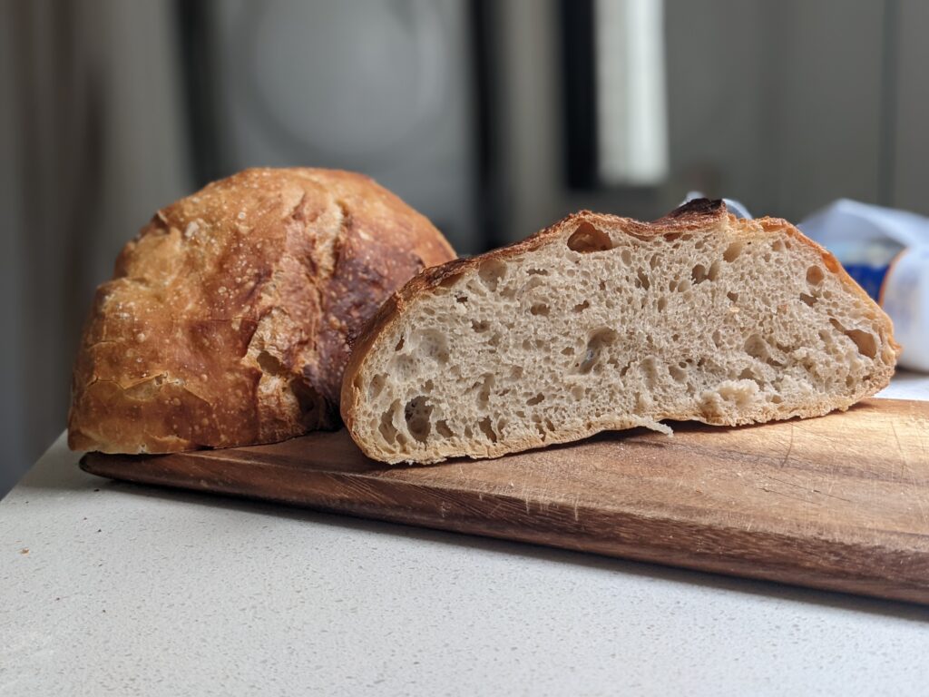 No knead Dutch oven bread sliced open on a wooden board showing the open crumb and crispy crust