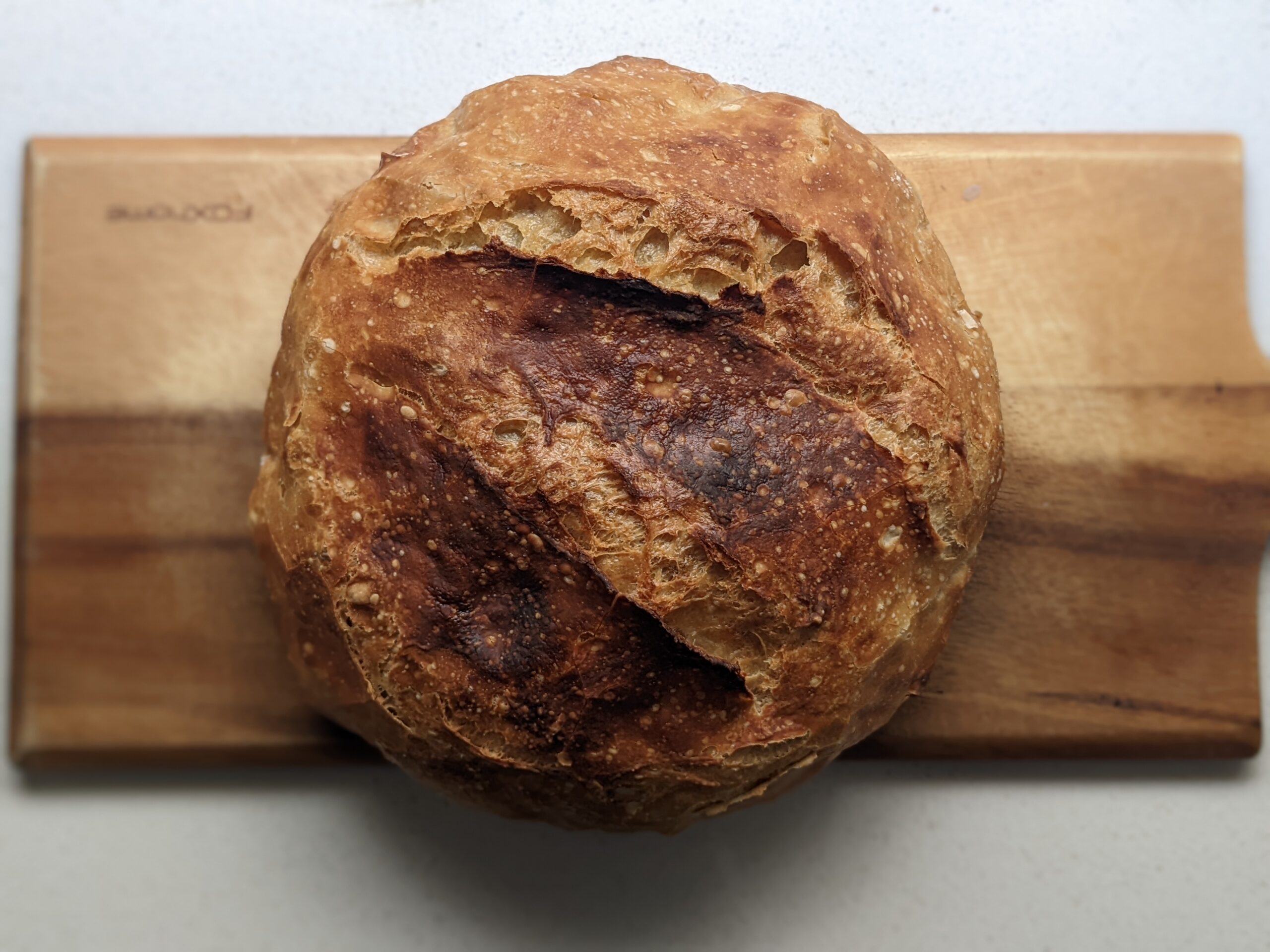 No knead Dutch oven bread whole loaf on a wooden board showing the scored crust after baking