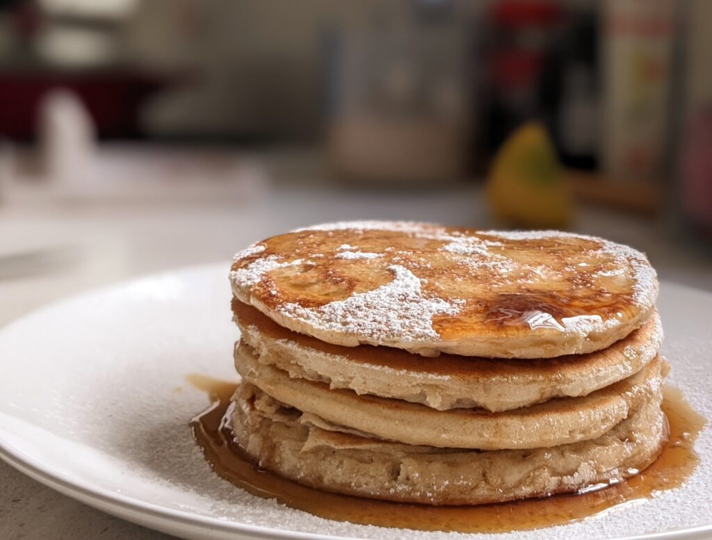 Stack of low calorie oat pancakes with maple syrup and powdered sugar on a white plate