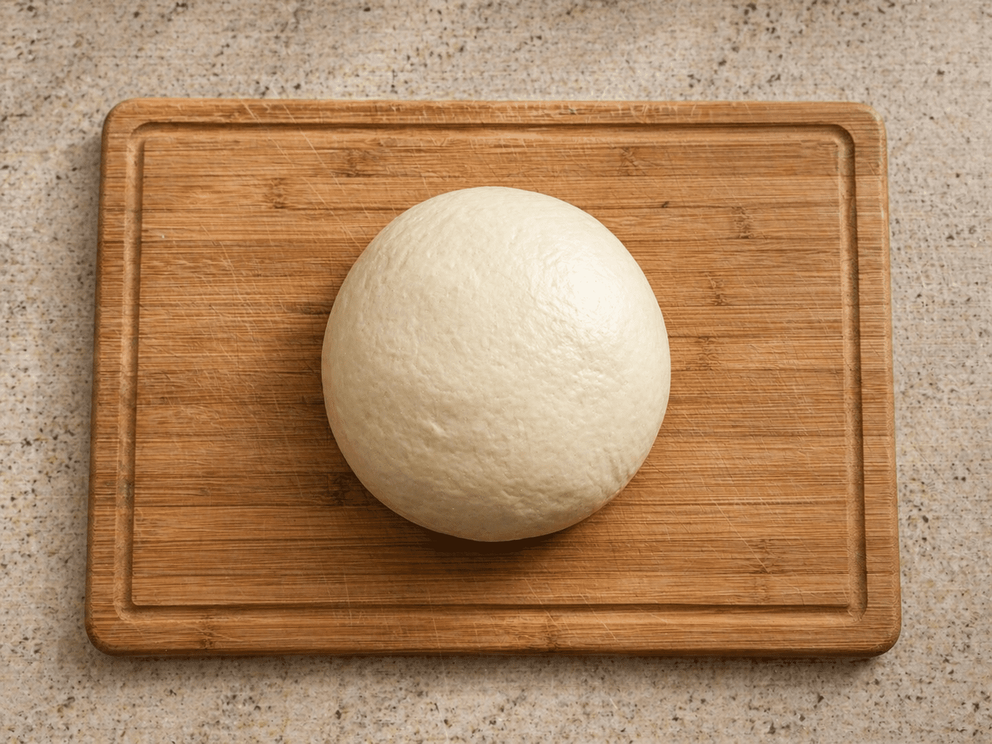Smooth Japanese milk bread dough shaped into a ball on a wooden cutting board before proofing