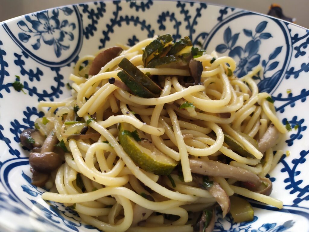 mushroom and zucchini pasta recipe served in a blue bowl with parsley and mixed mushrooms