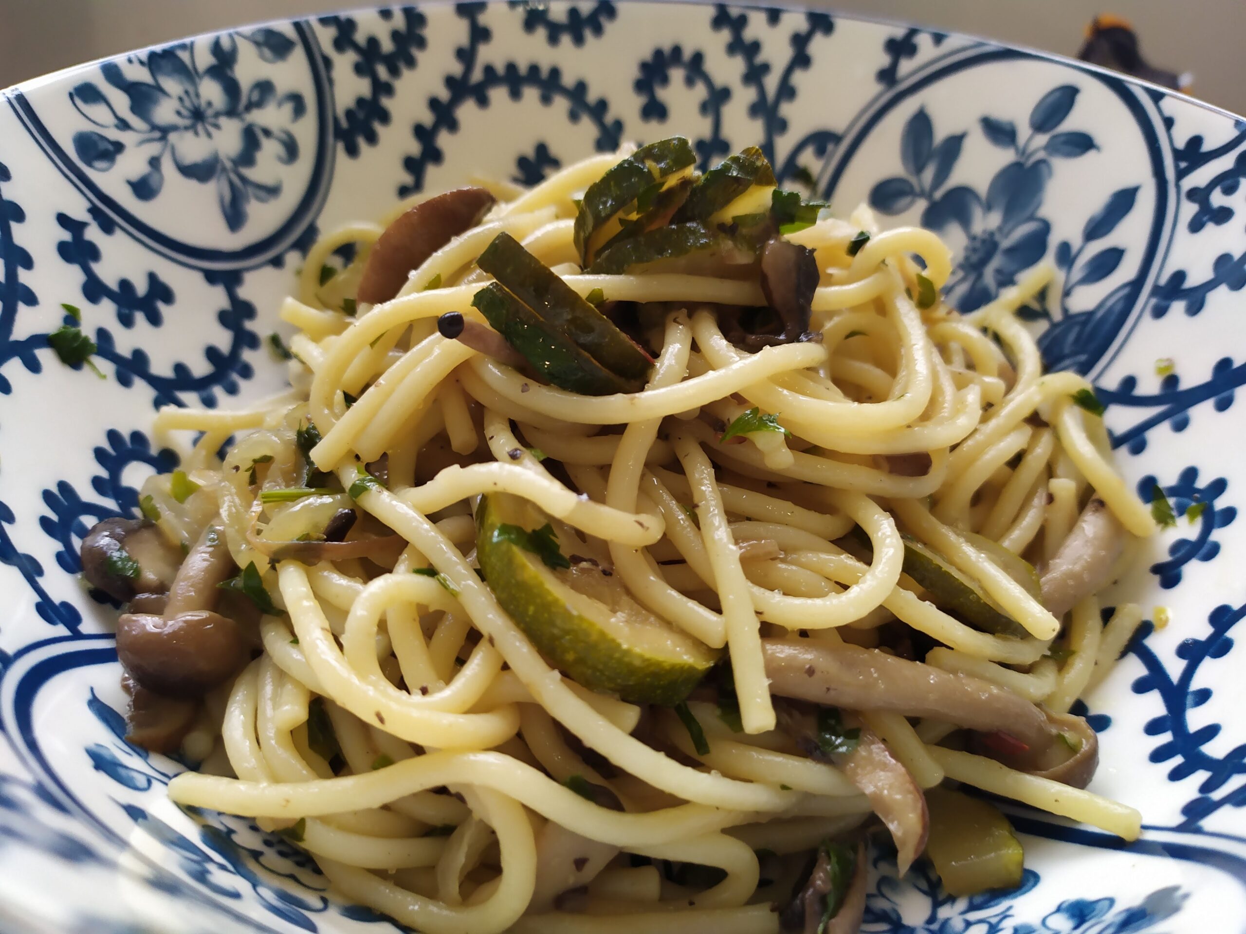 Mushroom and zucchini pasta recipe served in a blue bowl with parsley and mixed mushrooms