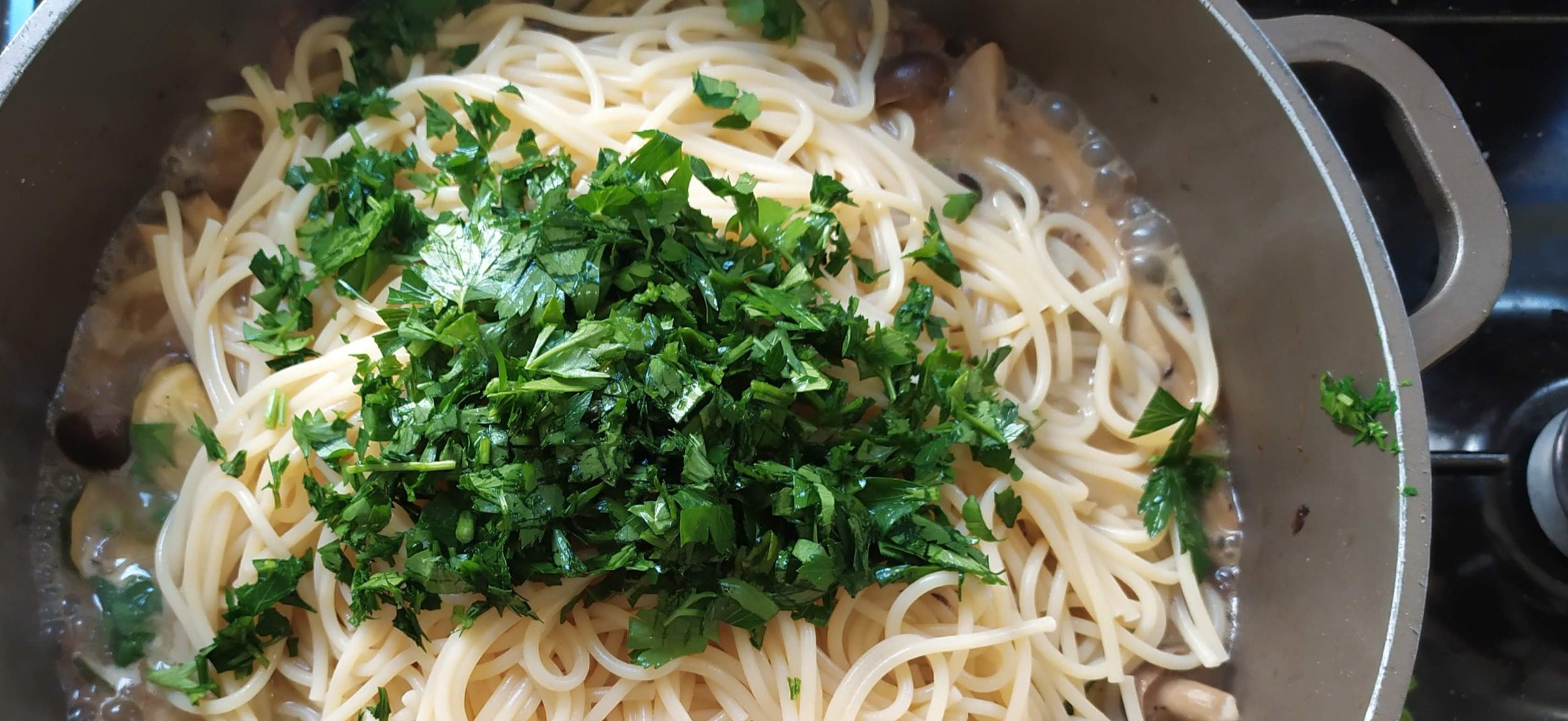 Spaghetti being tossed with fresh parsley and mushrooms in a pan