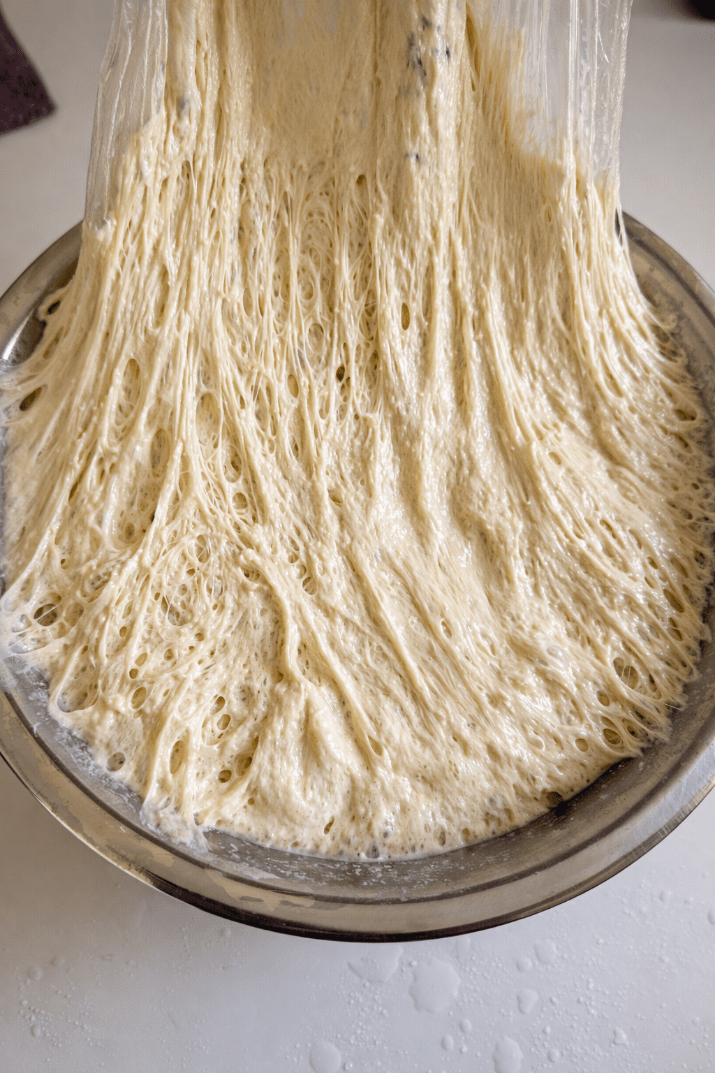 Fermented no knead bread dough falling from bowl showing well developed gluten strands