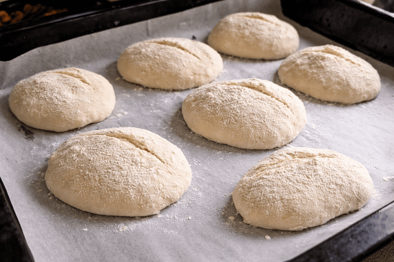 Shaped no knead bread buns dusted with flour on a baking tray lined with parchment paper