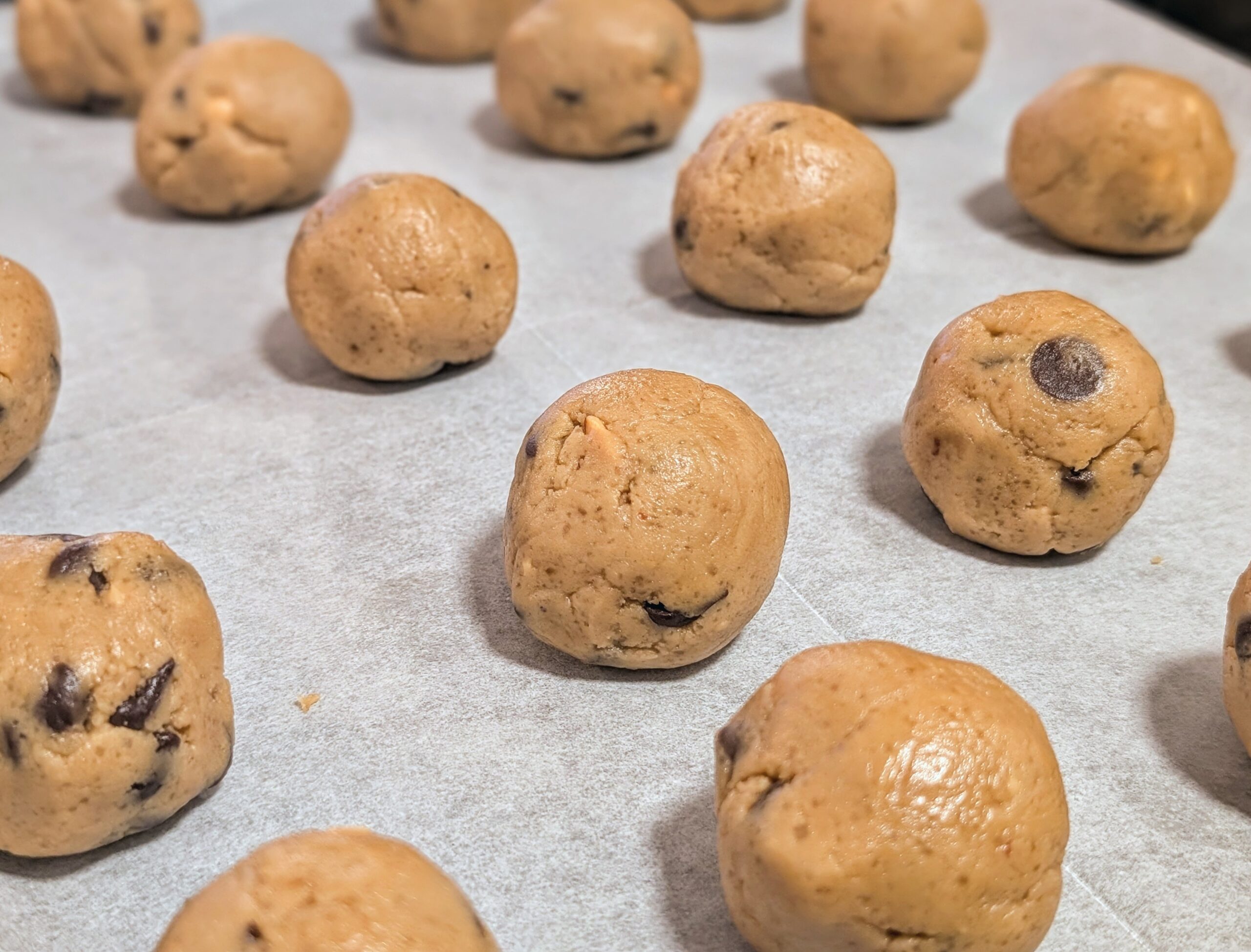 Peanut butter chocolate chip cookie dough balls lined up on a parchment-lined baking tray ready to bake