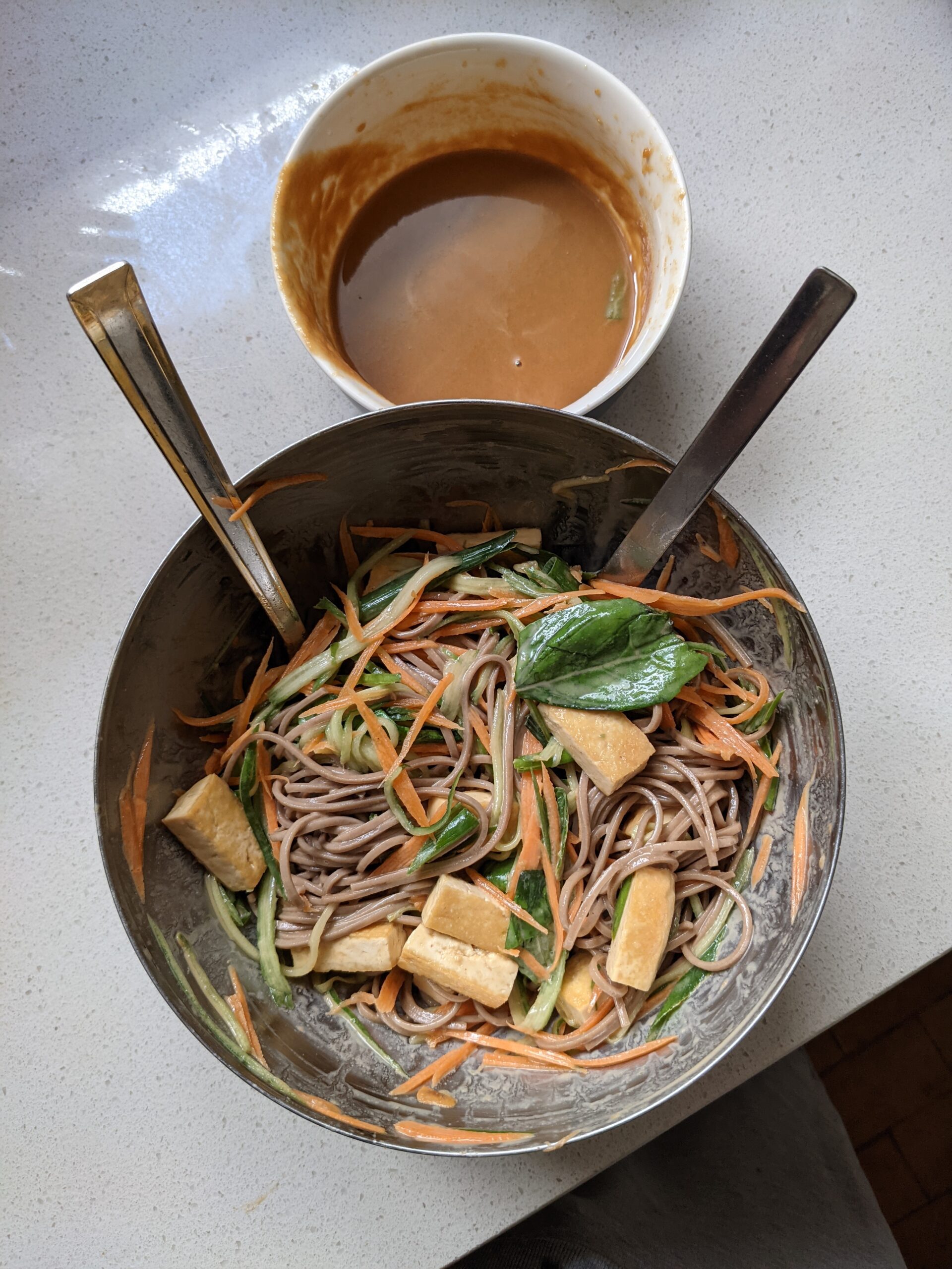 Soba noodle salad in a mixing bowl with peanut butter tahini dressing in a bowl on the side