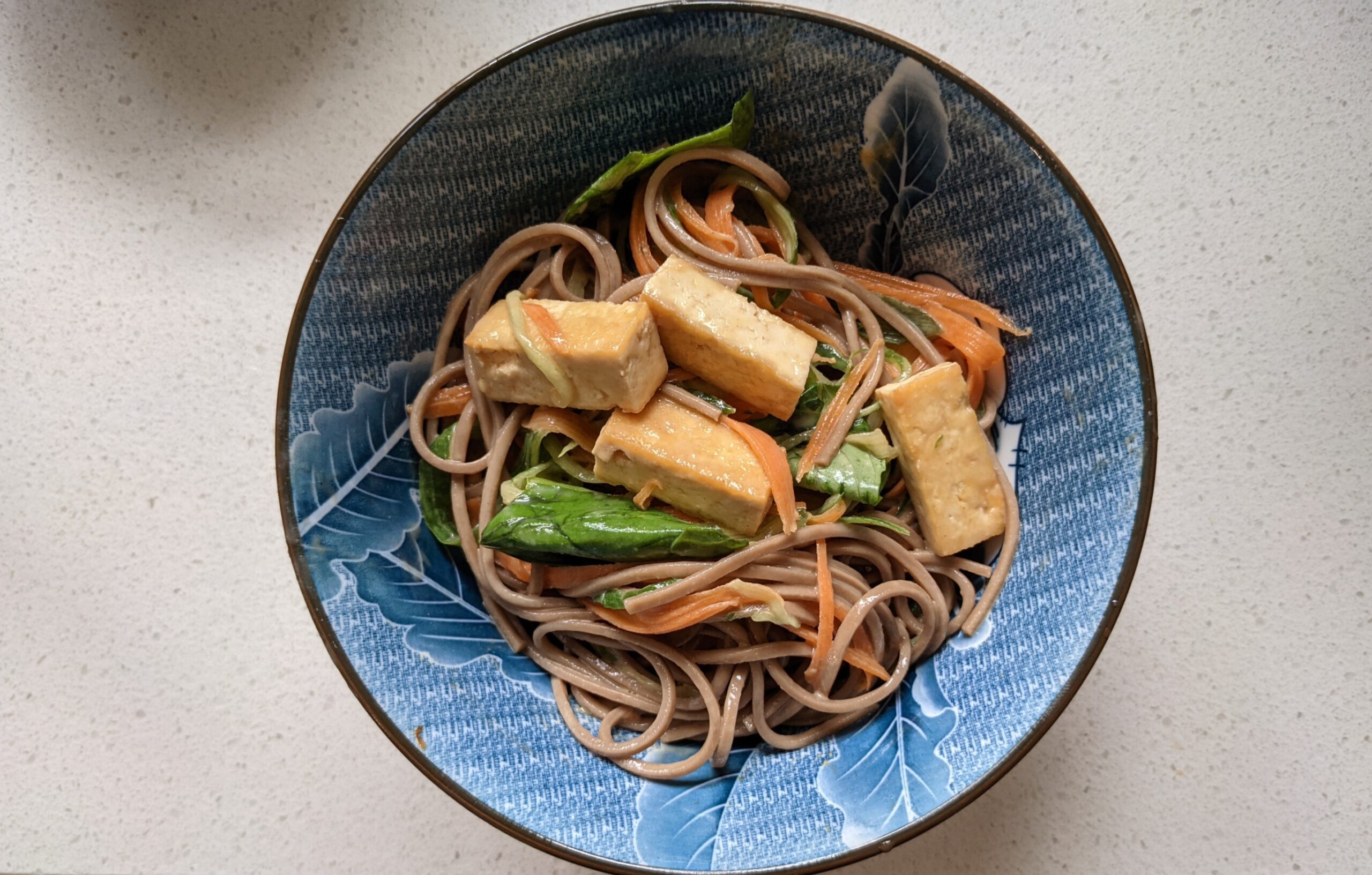 Peanut butter tahini soba noodle salad in a blue bowl with tofu, carrot and basil