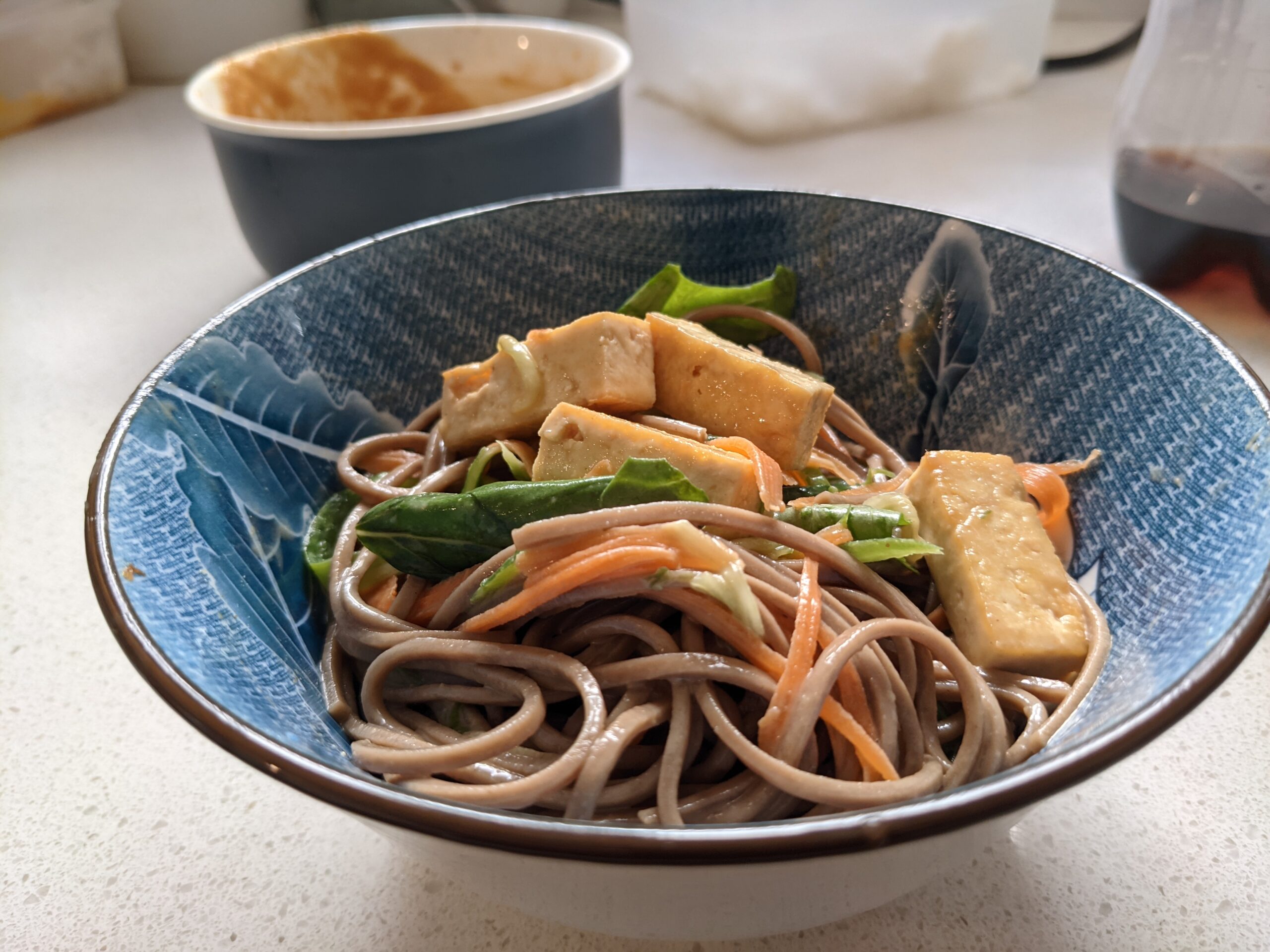 Peanut butter tahini soba noodle salad served in a blue bowl with crispy tofu and fresh basil