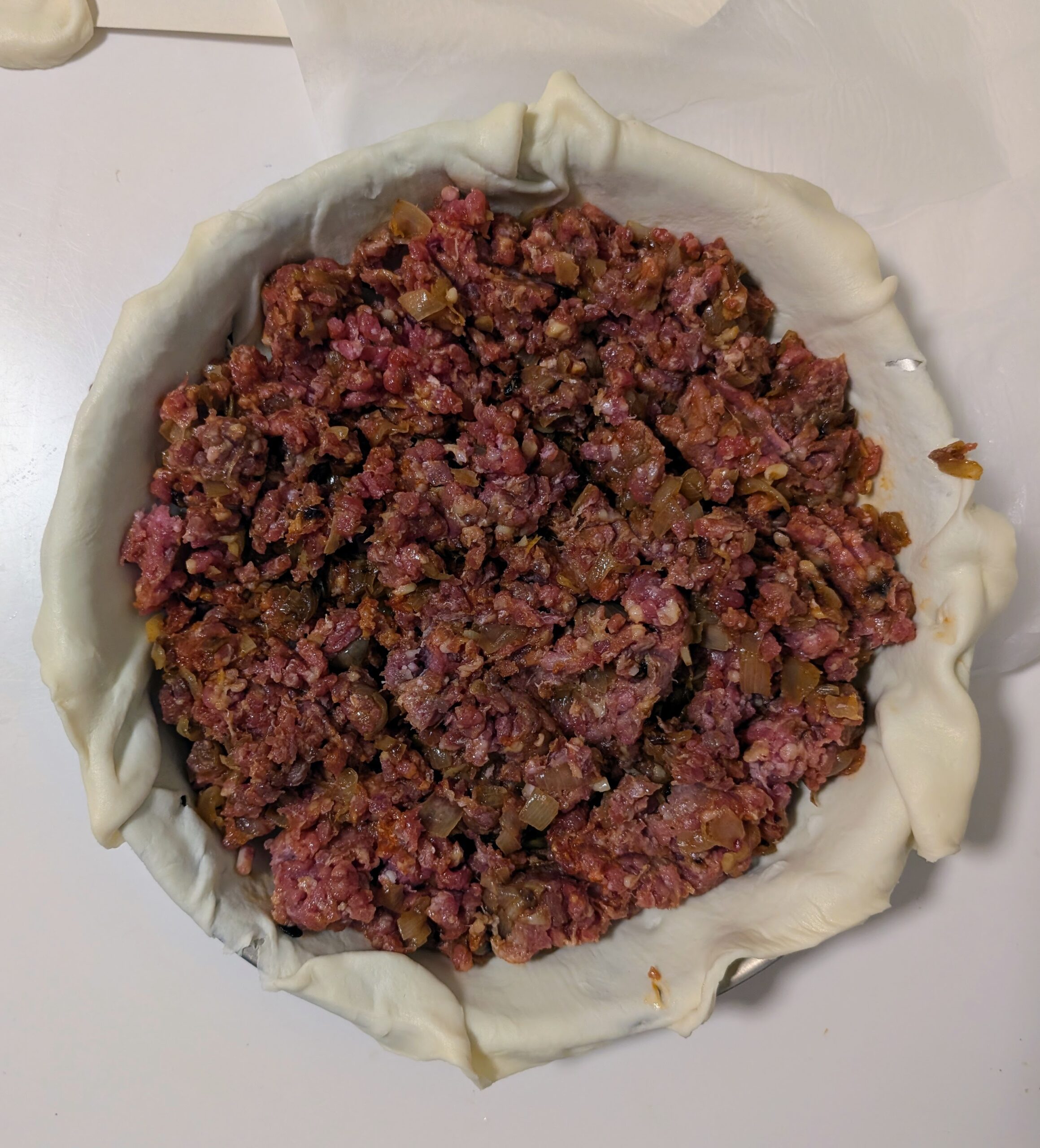 Raw ground beef and caramelised onion filling inside a puff pastry lined baking tray