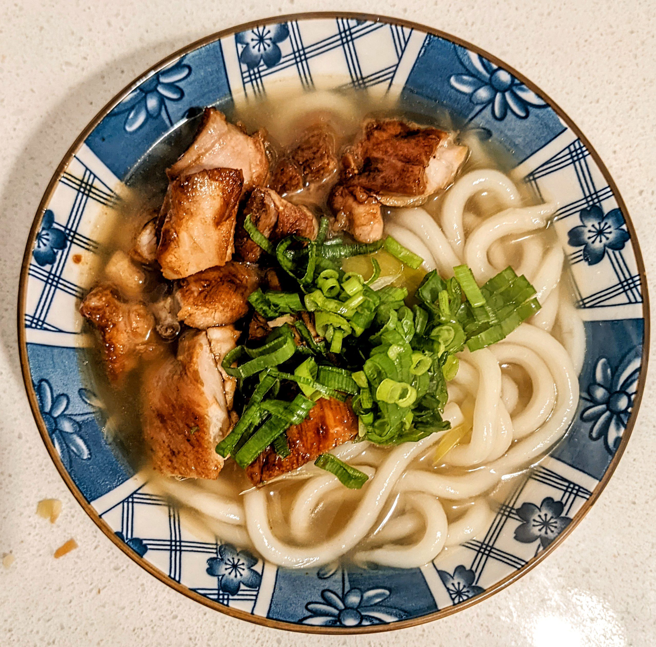 Overhead view of udon noodle chicken soup in a blue Japanese bowl with glazed chicken and green onions