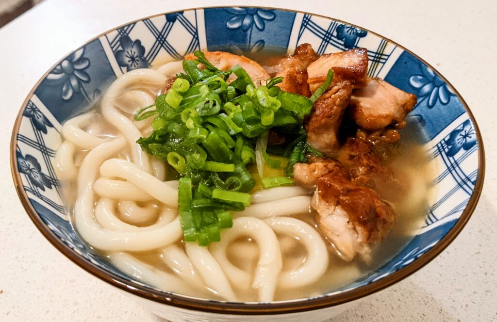 Udon noodle chicken soup in a blue Japanese bowl with glazed chicken and green onions