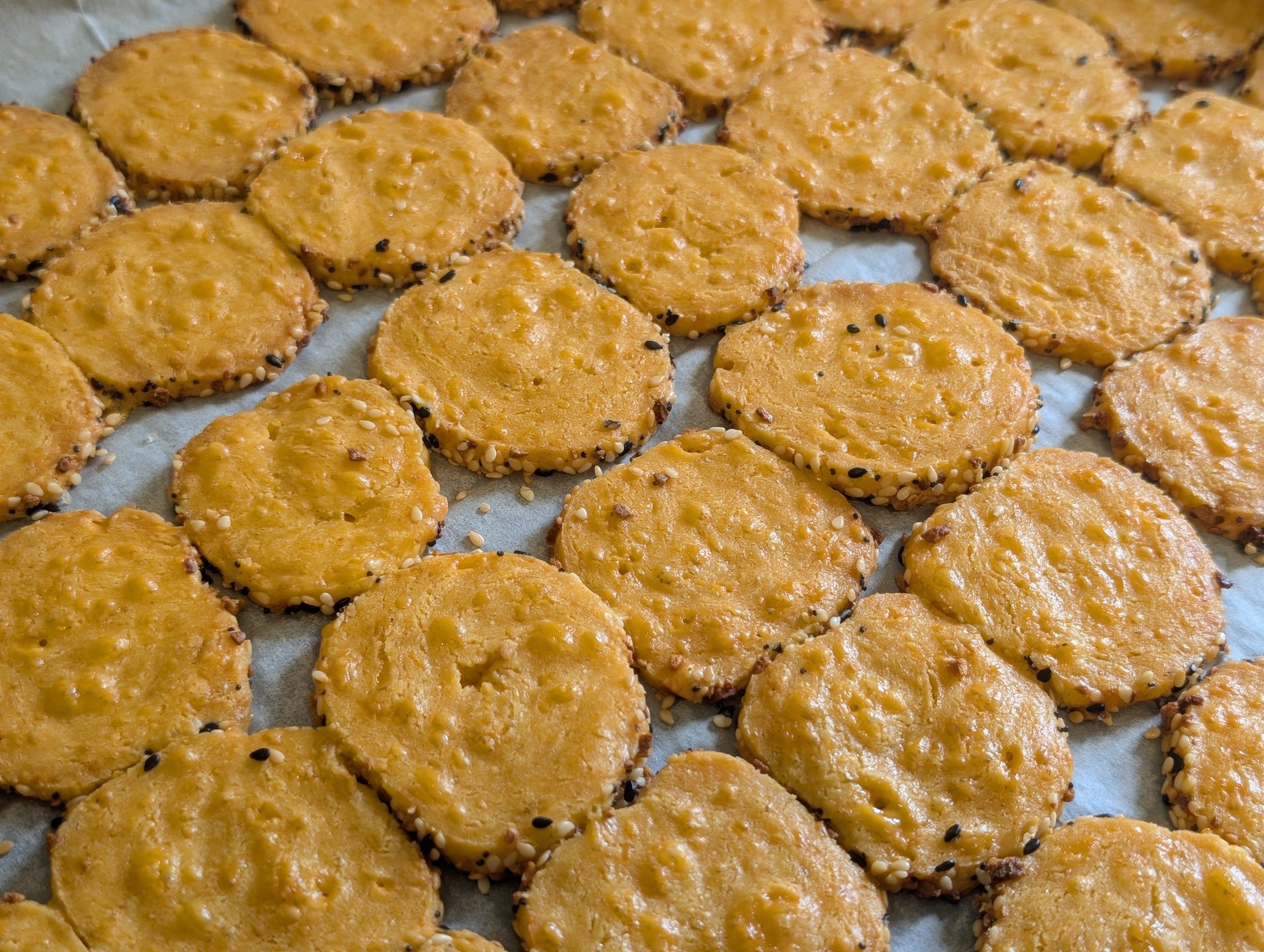 Top-down view of baked cheddar cheese crackers on parchment paper, golden with everything bagel seeded edges