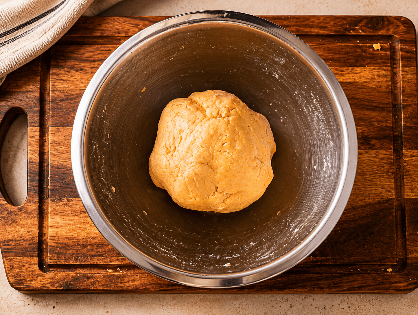 Smooth orange cheddar cracker dough formed into a ball in a metal bowl on a wooden board