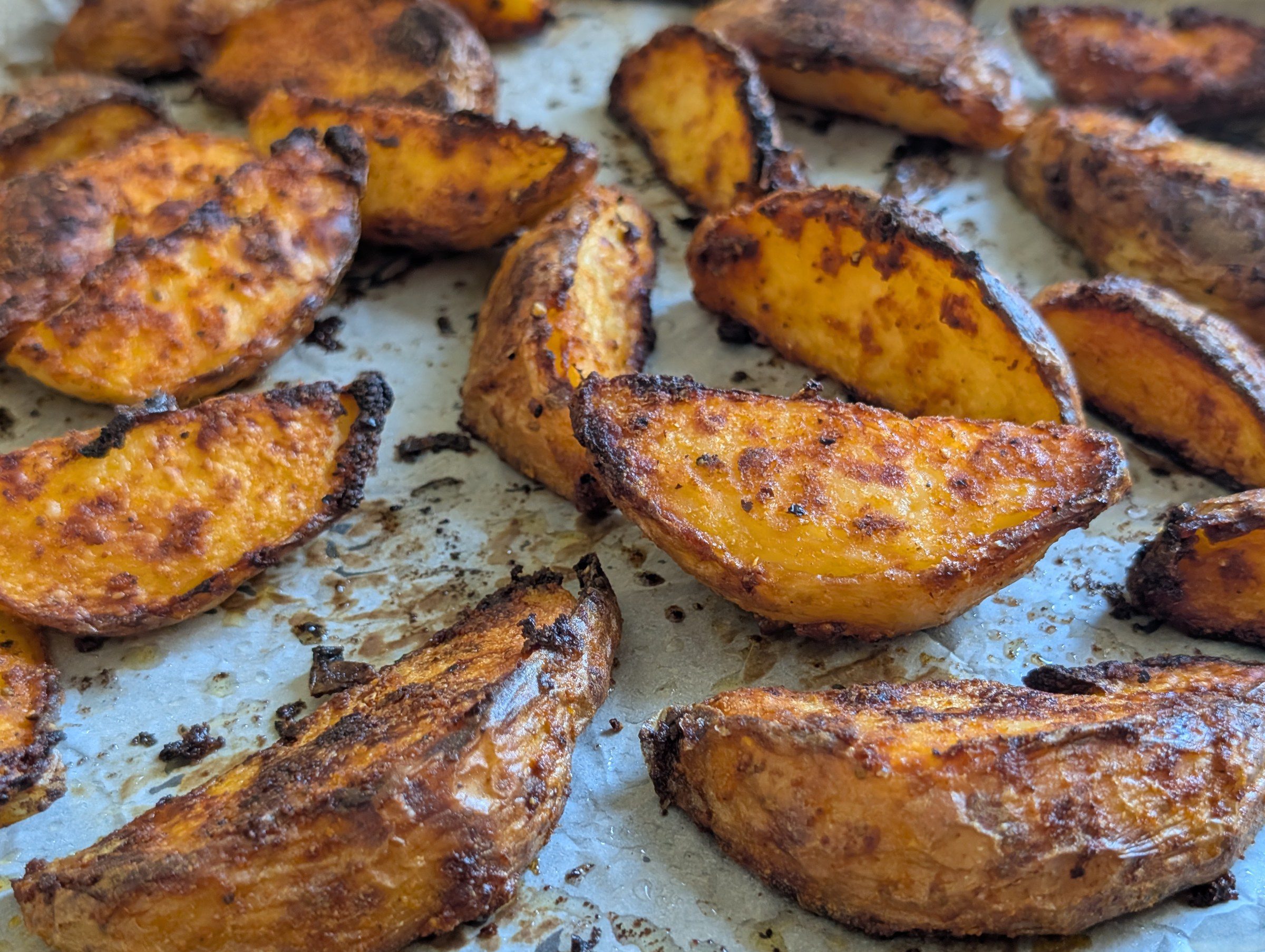 Close-up of golden crispy baked potato wedges with charred edges on parchment paper