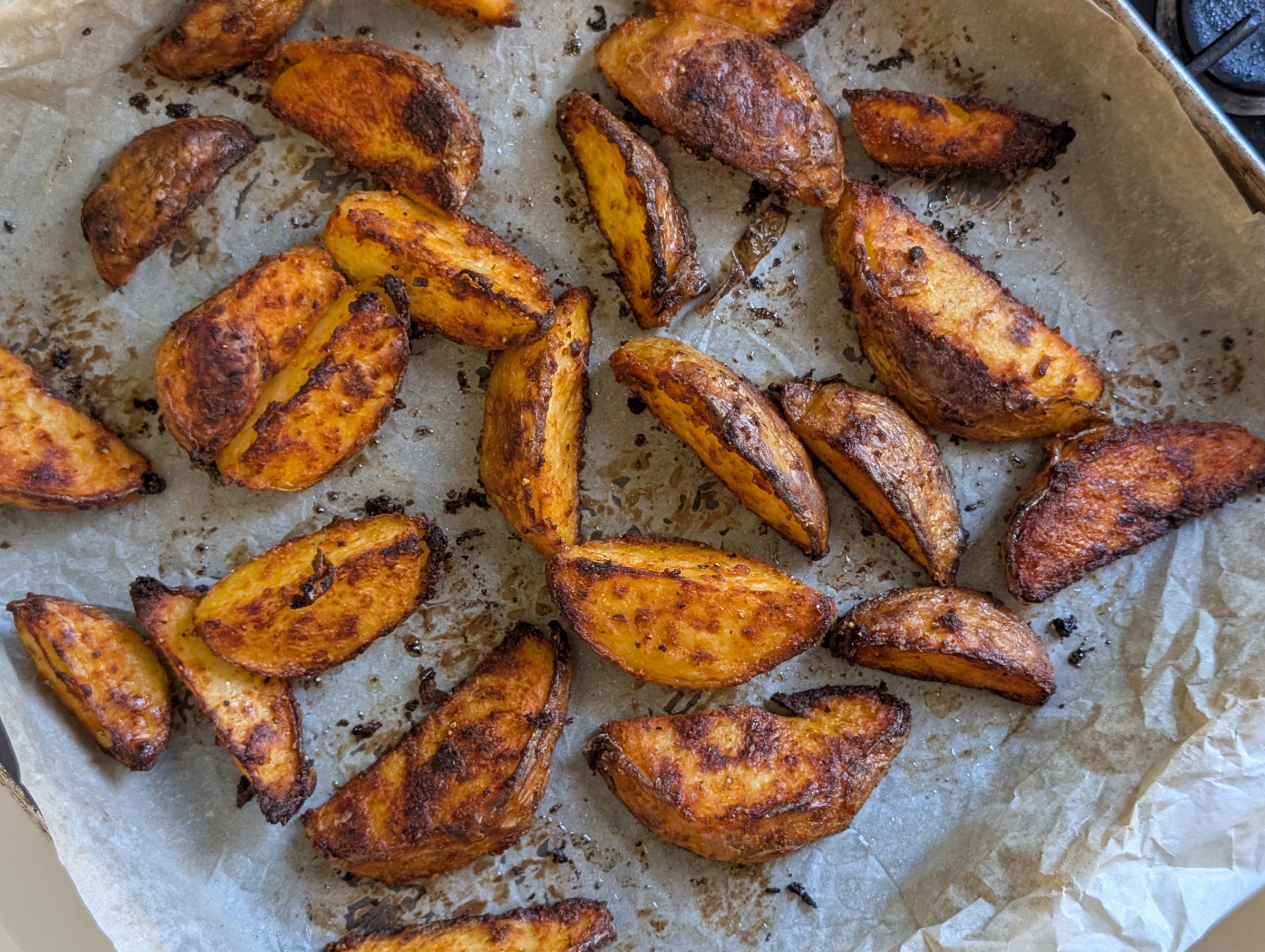 Crispy baked potato wedges golden brown on a parchment-lined baking tray, overhead view