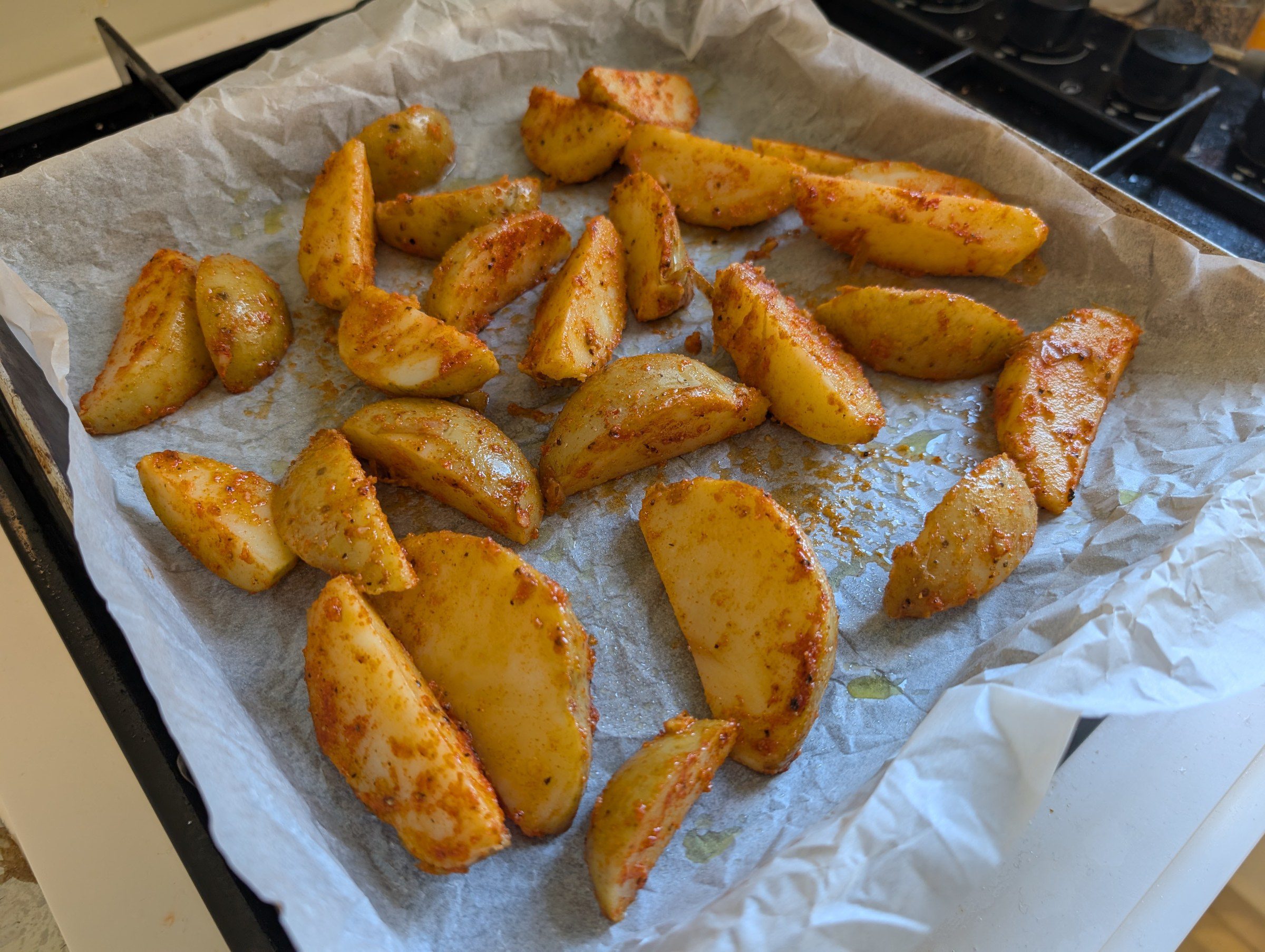 Raw seasoned potato wedges spread on a parchment-lined baking tray ready to bake