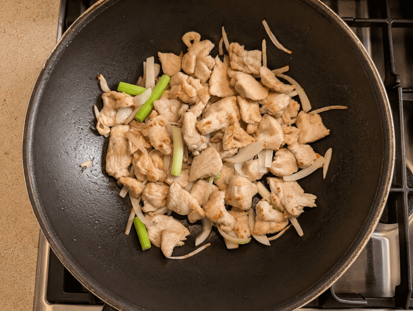 Chicken pieces stir-frying in the wok with sliced white onion and green onions