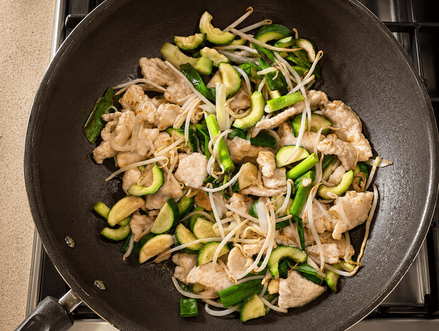 Chicken, zucchini, bean sprouts and aromatics combined in the wok before noodles and sauce are added