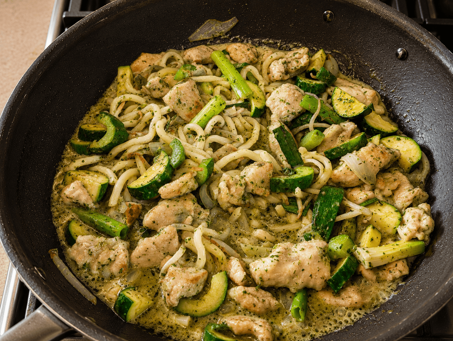Close-up of finished green curry noodle stir fry with udon noodles, chicken and zucchini glossy with bright green coconut-cilantro sauce