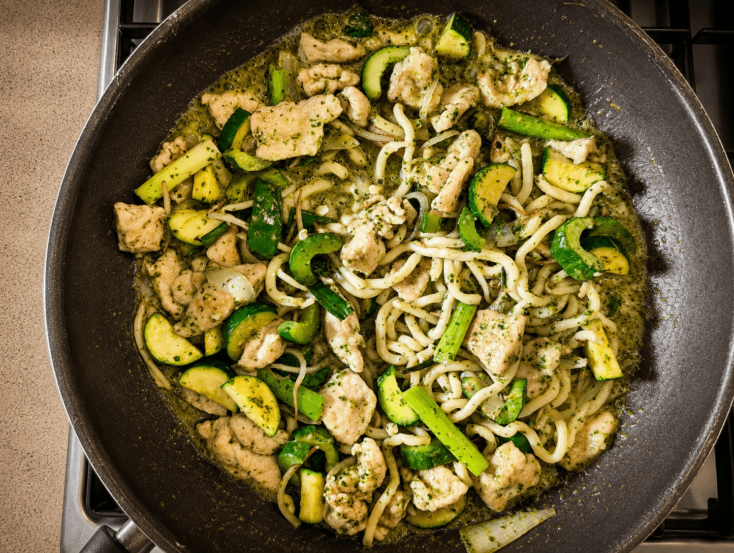 Green curry noodle stir fry in a wok with chicken, zucchini, bean sprouts and udon noodles coated in bright green coconut-cilantro sauce