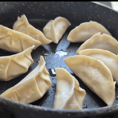 Animated GIF of cornflour-water slurry being poured into a hot pan with gyoza, sizzling dramatically