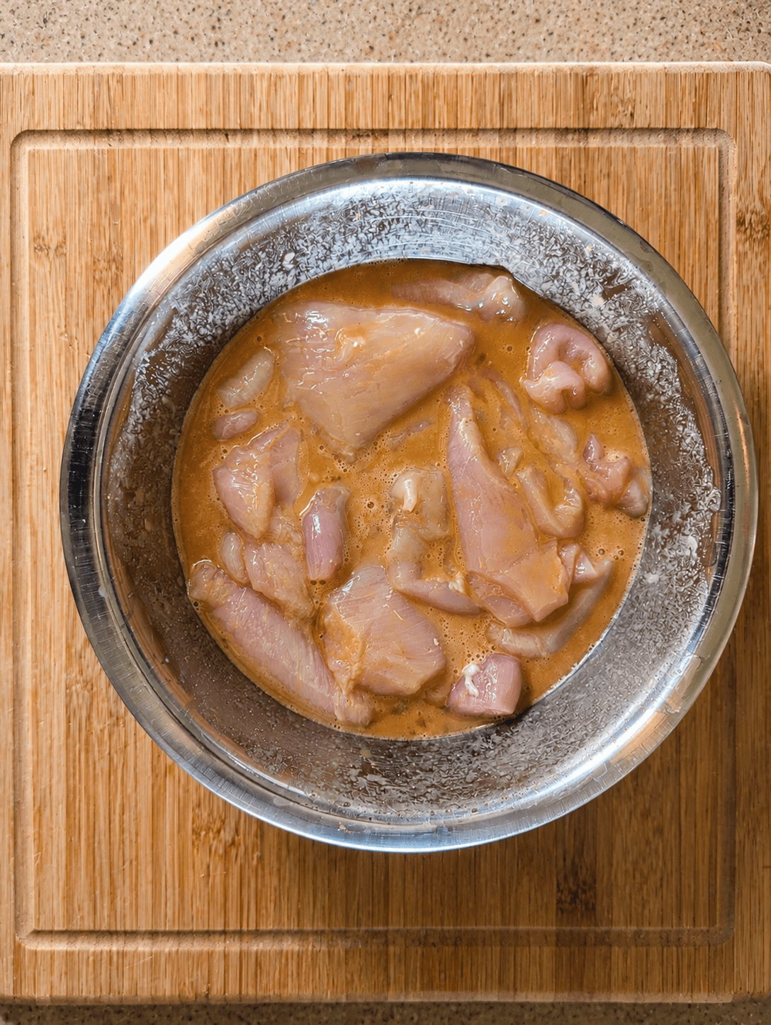 Thin chicken cutlets submerged in a golden honey-mustard egg marinade in a metal bowl on a wooden cutting board