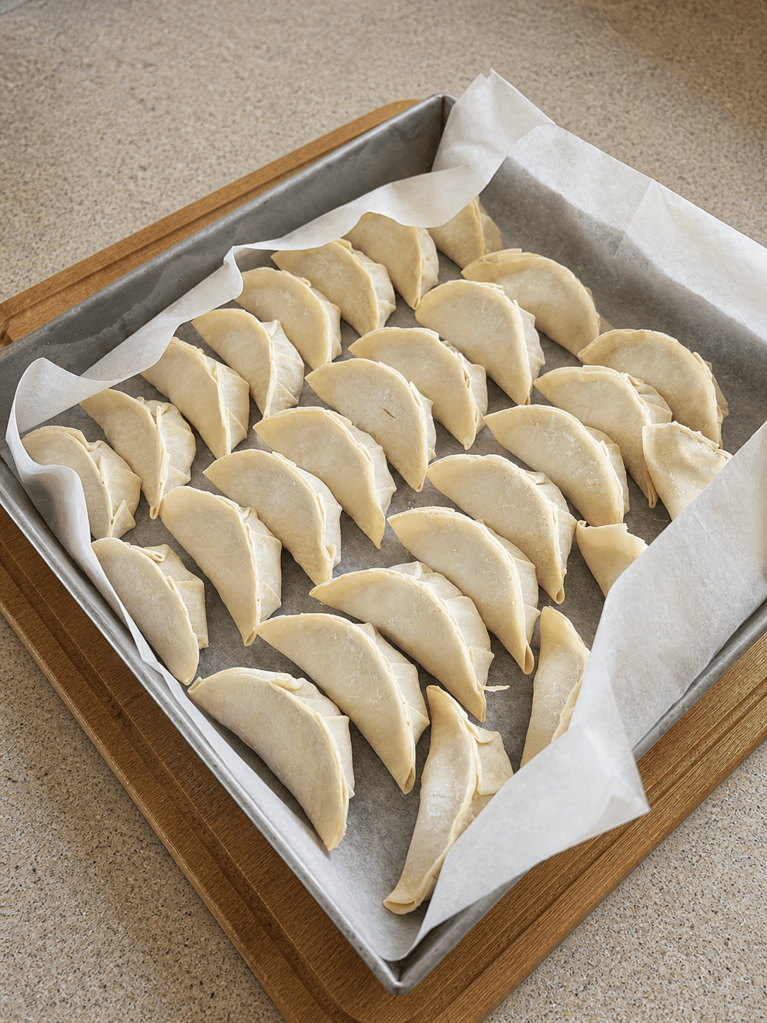 Raw shaped gyoza arranged on a parchment-lined baking tray, ready to be frozen