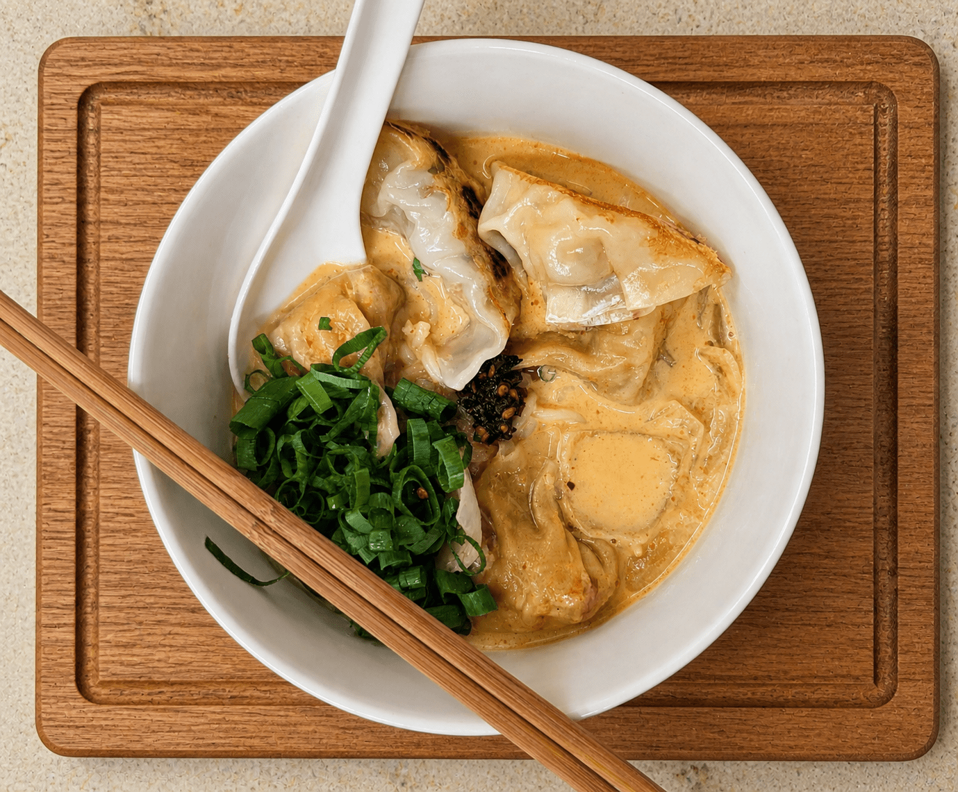Japanese gyoza in a bowl of red curry coconut noodles topped with green onion
