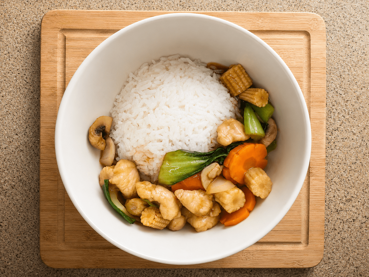 Oyster sauce chicken stir fry served in a white bowl over steamed white rice on a wooden cutting board