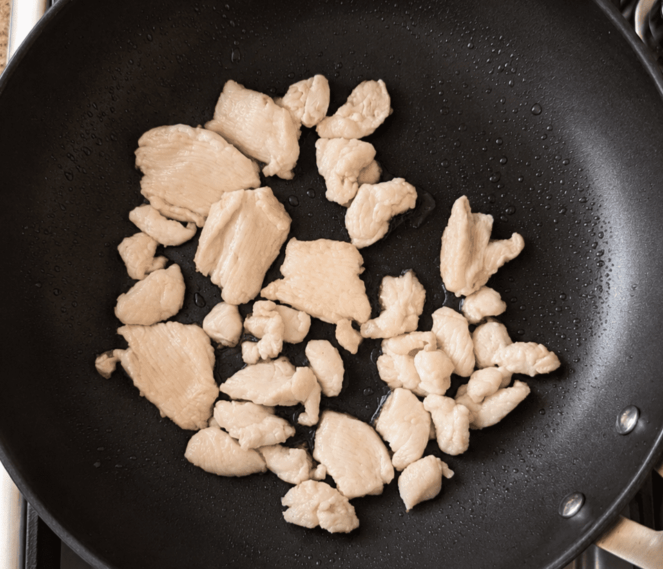 Thinly sliced raw chicken pieces coated in corn flour, searing in a hot non-stick pan