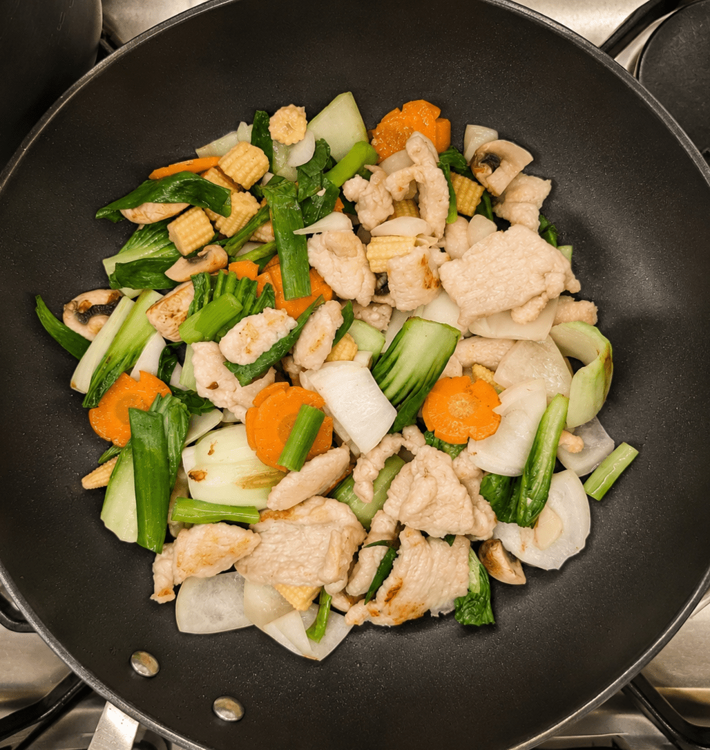 Stir-fried chicken, bok choy, carrots, mini corn and mushrooms all combined together in a wok before the sauce is added