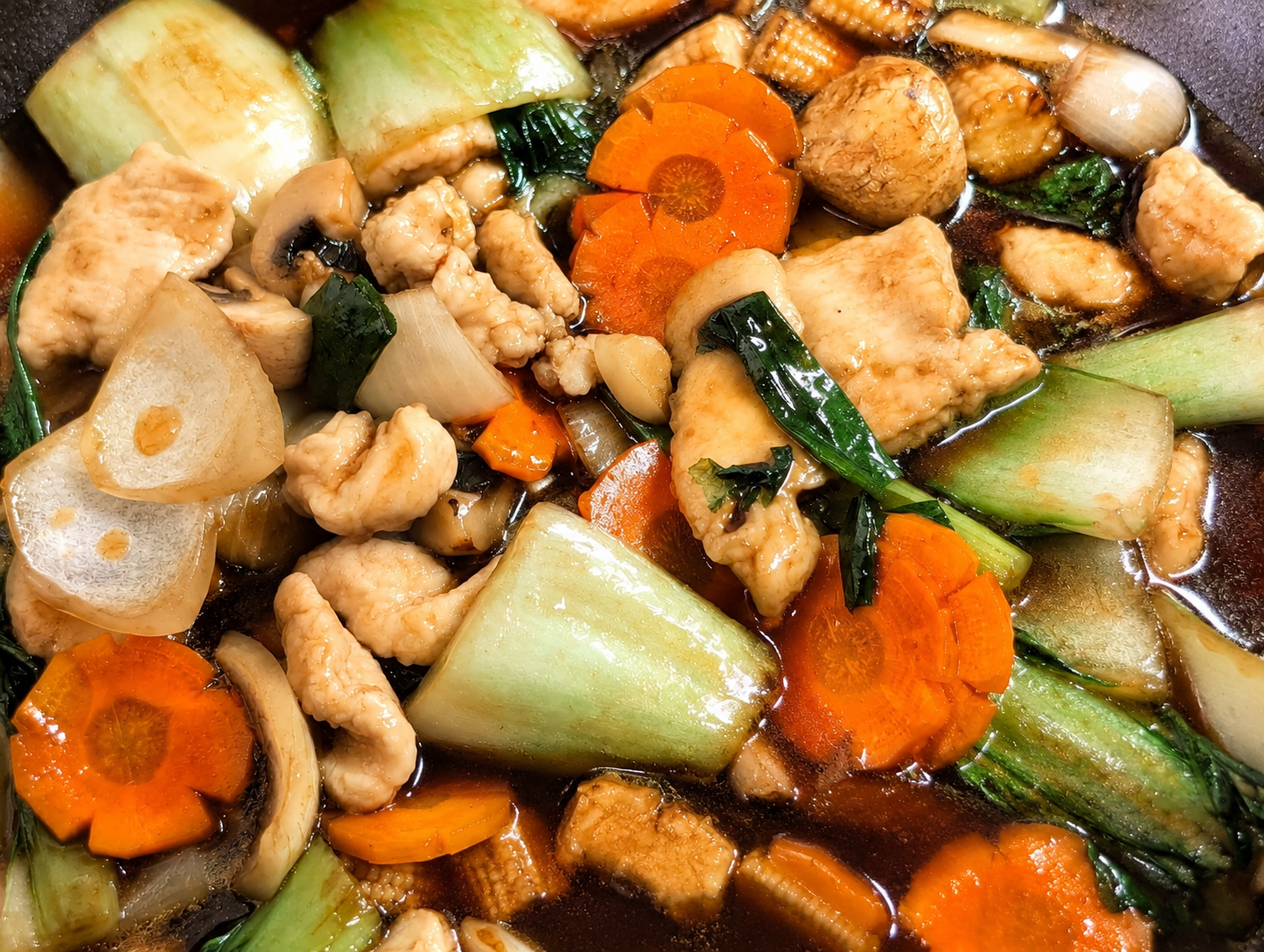 Oyster sauce chicken stir fry in a wok with bok choy, carrots, mini corn, mushrooms and tender chicken in a glossy dark sauce