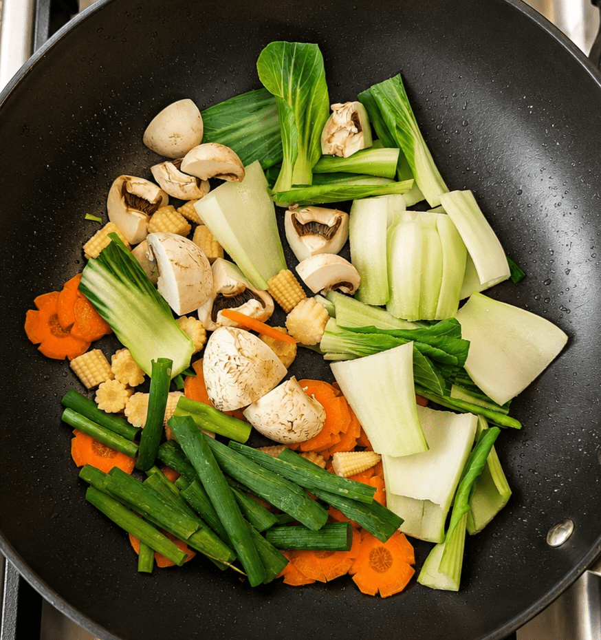 Sliced carrots, bok choy, mini corn, mushrooms and green onions stir-frying in a hot wok