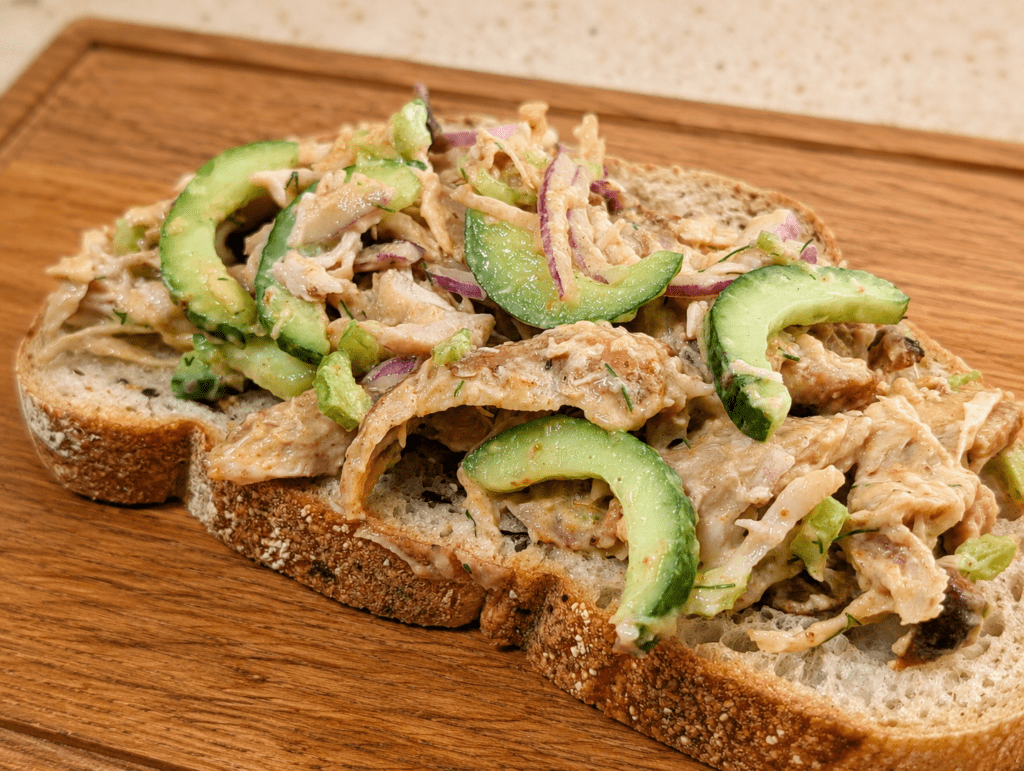 Open-faced leftover rotisserie chicken salad sandwich on dark seeded bread with cucumber and red onion