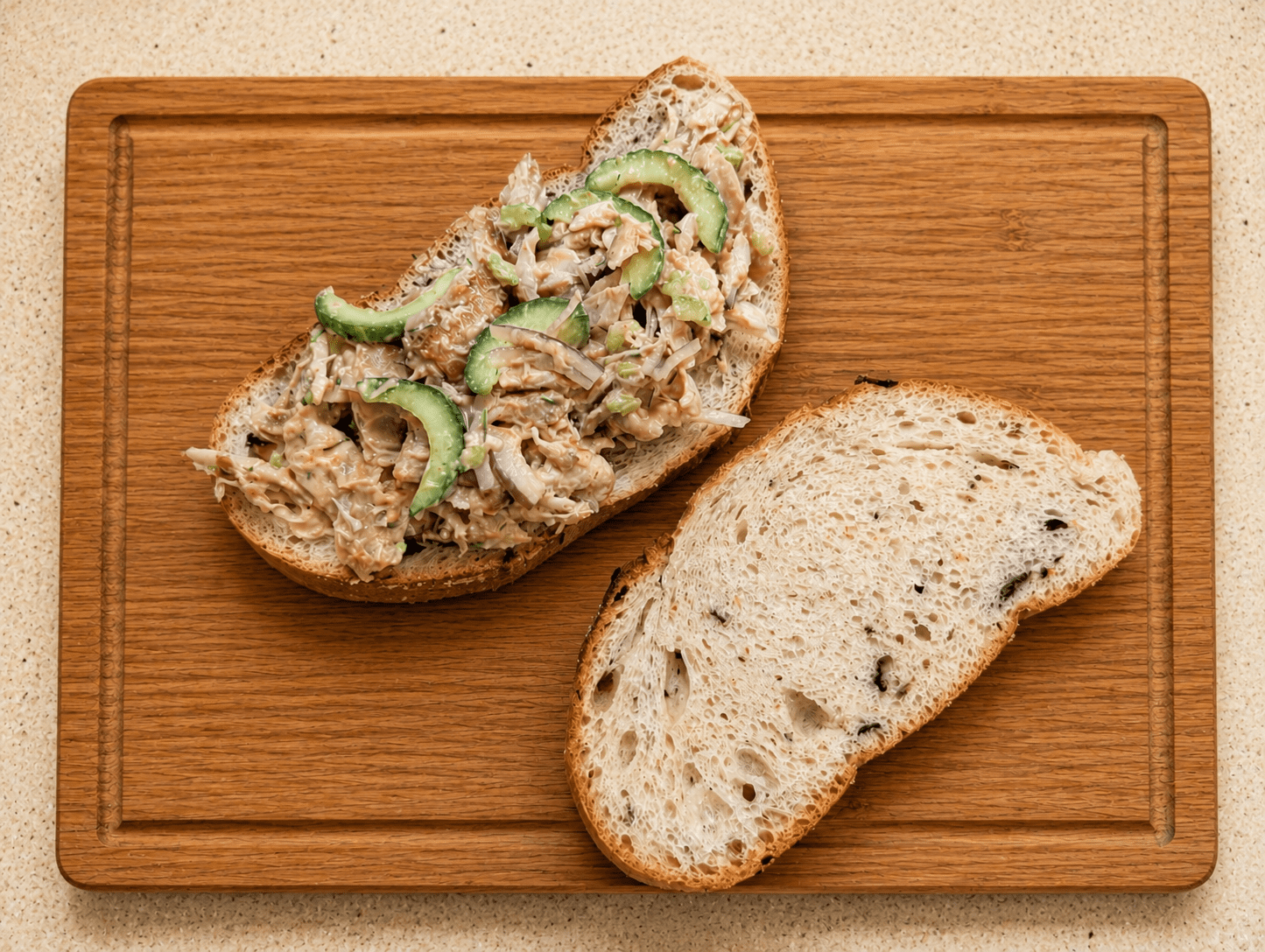 Top-down view of an open-faced leftover rotisserie chicken salad sandwich next to a closed slice of bread on a wooden board