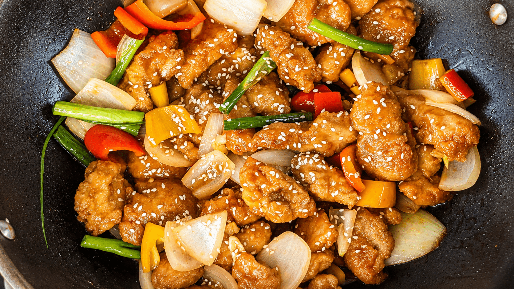Crispy sweet and sour chicken in a wok with bell peppers and sesame seeds
