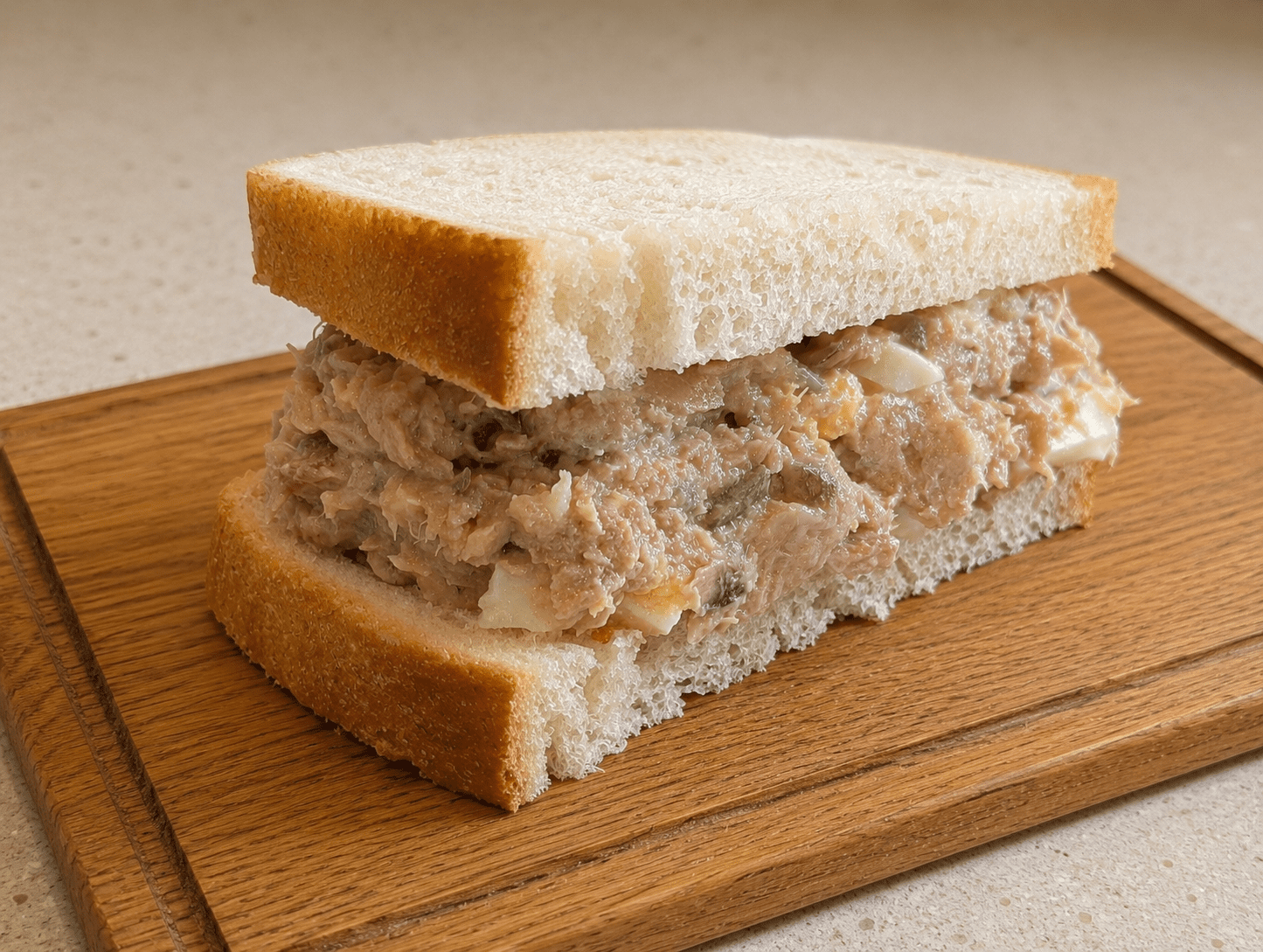 Homemade tuna salad sandwich on white bread sliced in half on a wooden board
