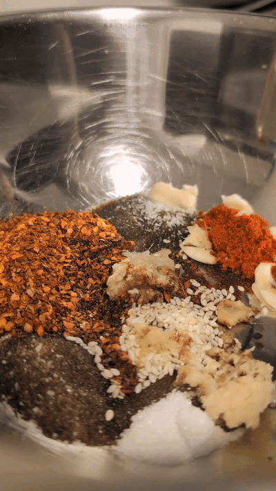 Animated GIF of hot oil being poured over chili flakes and aromatics in a bowl, sizzling and bubbling violently on contact