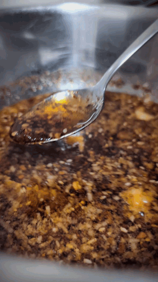 Animated GIF close-up of finished homemade chili oil being stirred in a bowl with a spoon showing the deep glossy red color