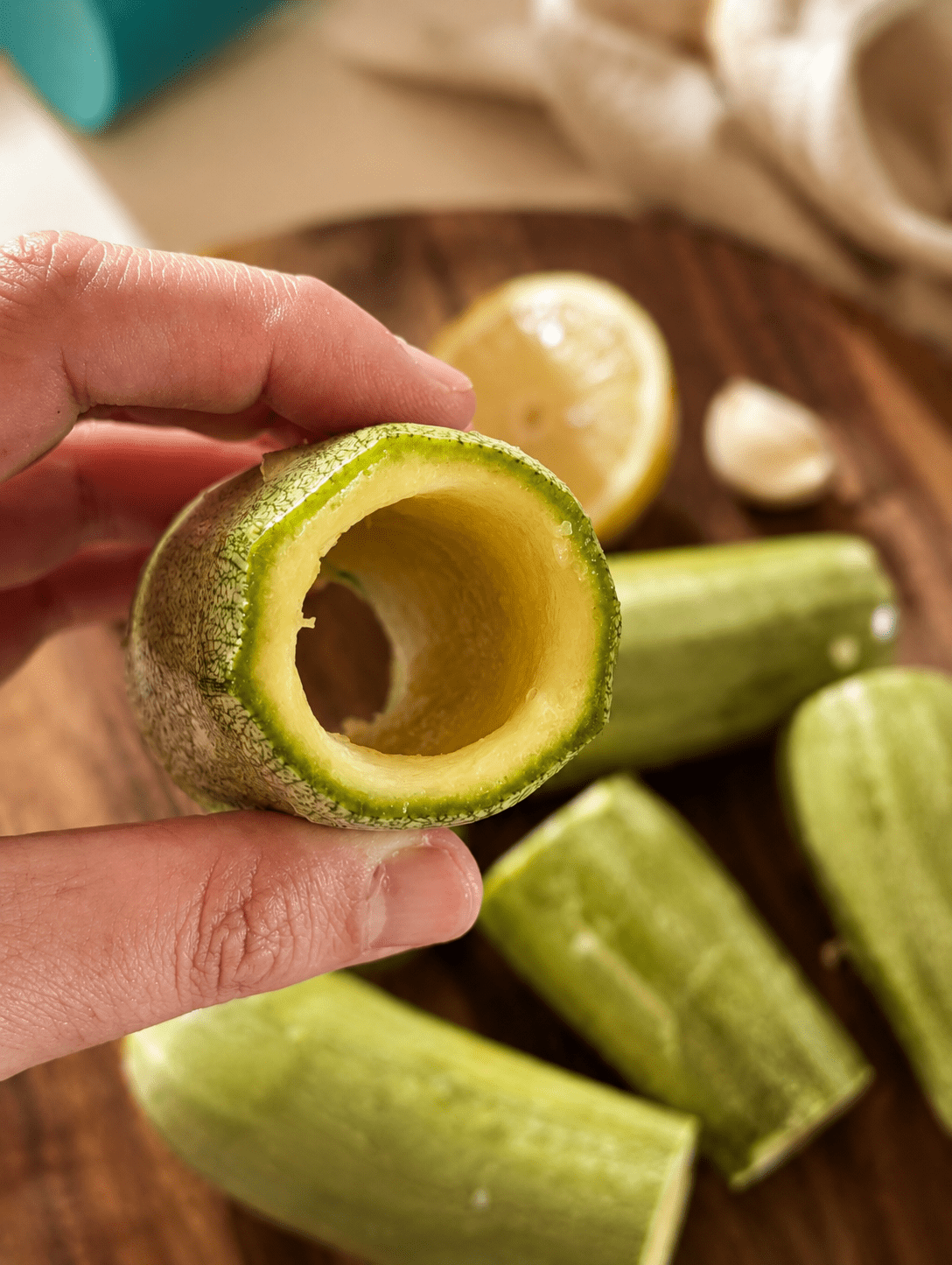 A zucchini cored into a hollow tube held by hand, showing the thin walls ready for stuffing