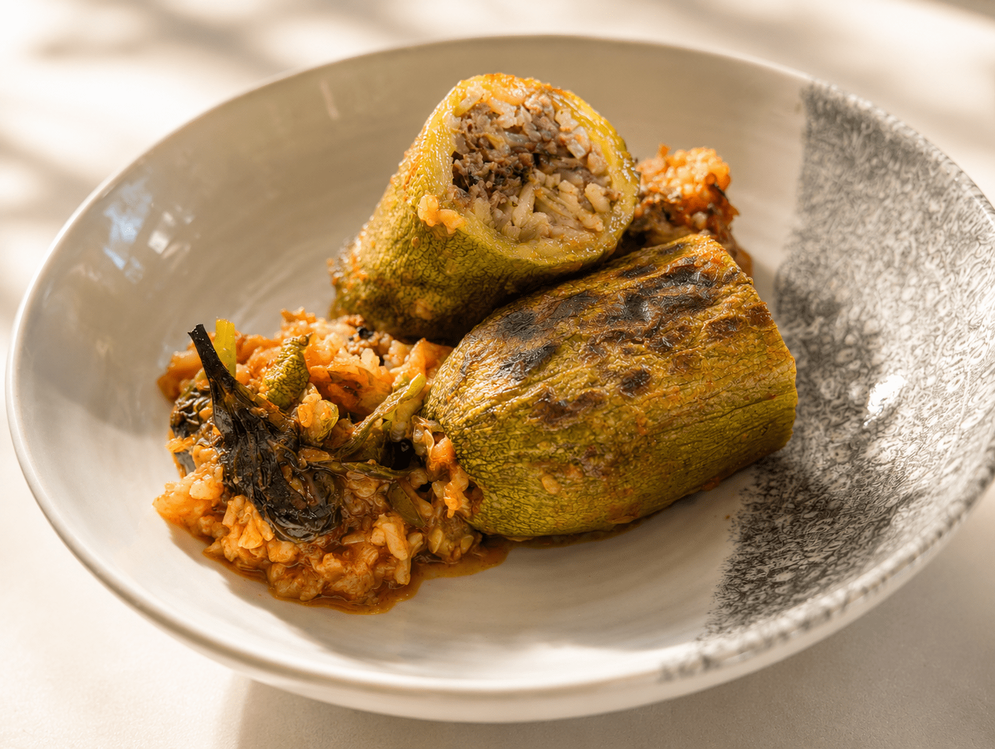 Middle Eastern stuffed zucchini cut open showing the beef and rice filling, served with tomato rice and sauce