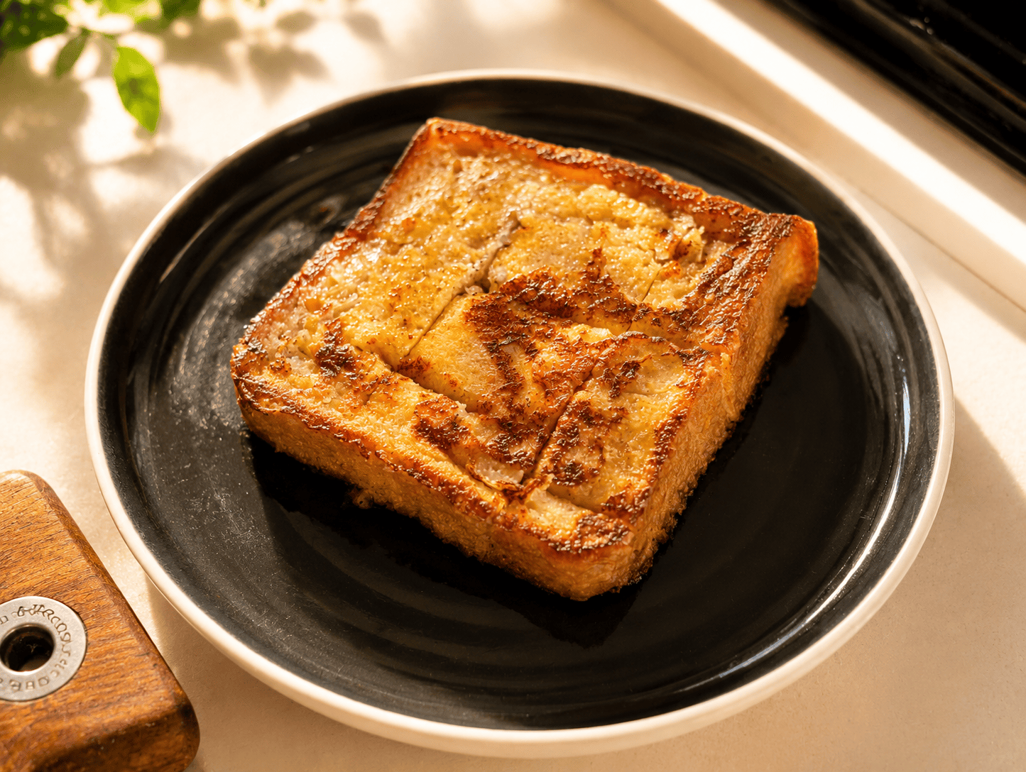 A thick slice of golden brown French toast on a dark plate, custardy inside with a caramelized crust