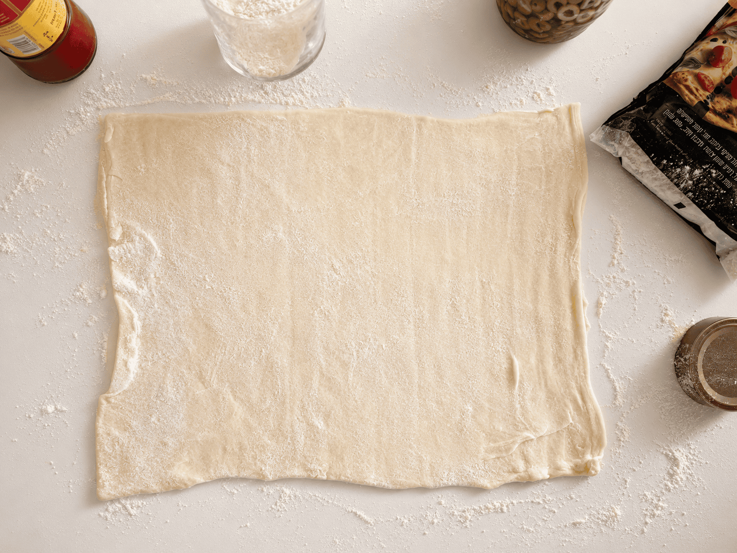 A sheet of puff pastry rolled out into a rectangle on a floured surface
